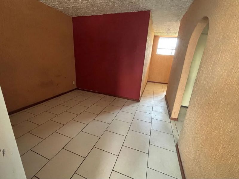 An empty living area featuring ceramic floor tiles, textured walls, and an arched entryway, presenting a blank canvas for renovation and interior design.