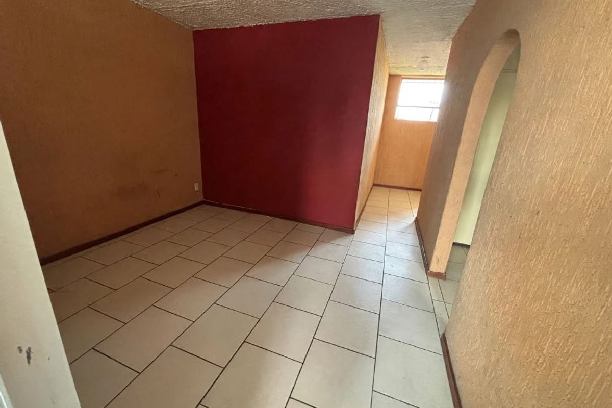 An empty living area featuring ceramic floor tiles, textured walls, and an arched entryway, presenting a blank canvas for renovation and interior design.