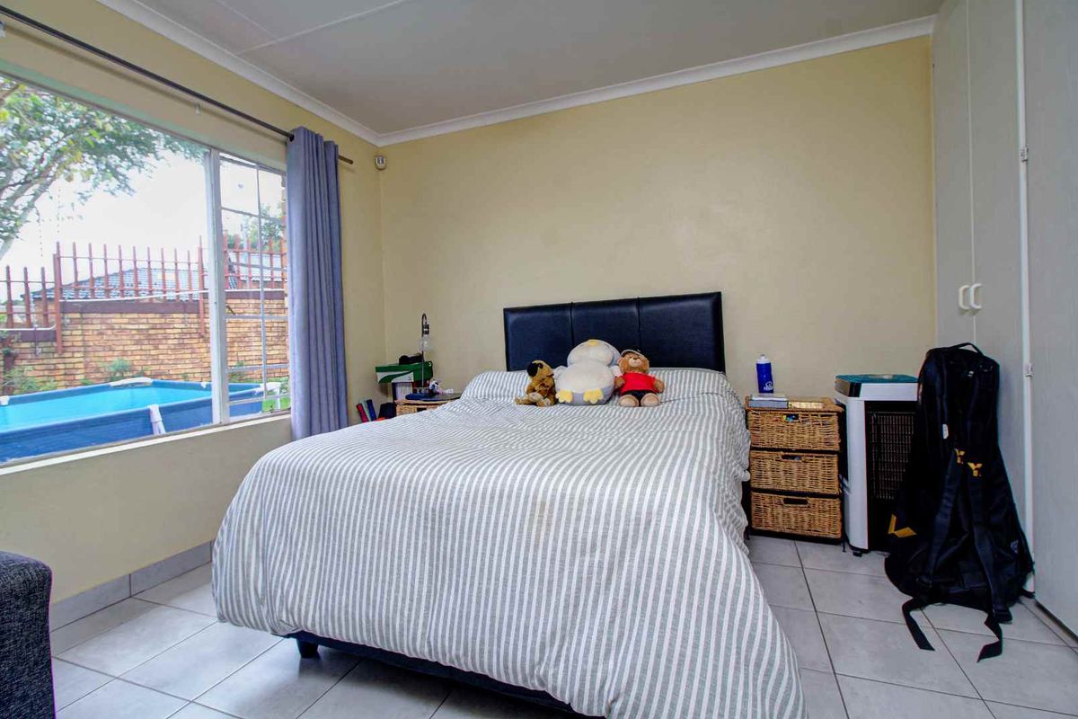 A bedroom featuring tiled flooring, built-in cupboards, and a large window overlooking the outdoor pool area.