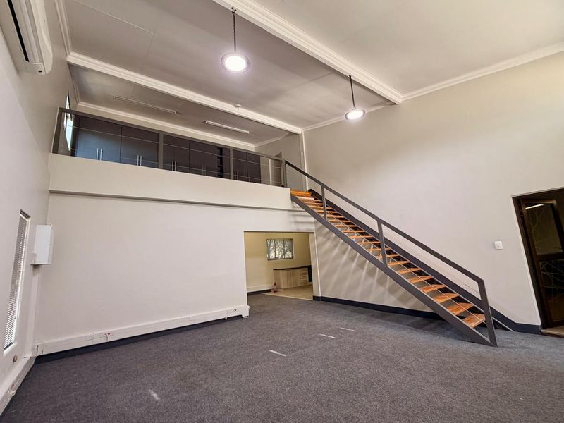 Spacious open-plan living area featuring a mezzanine level, metal staircase, and neutral finishes, offering a versatile layout for various living arrangements.