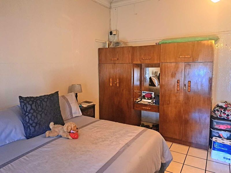 A bedroom featuring built-in wooden cupboards and tiled flooring, requiring cosmetic updates to the wall finishes.