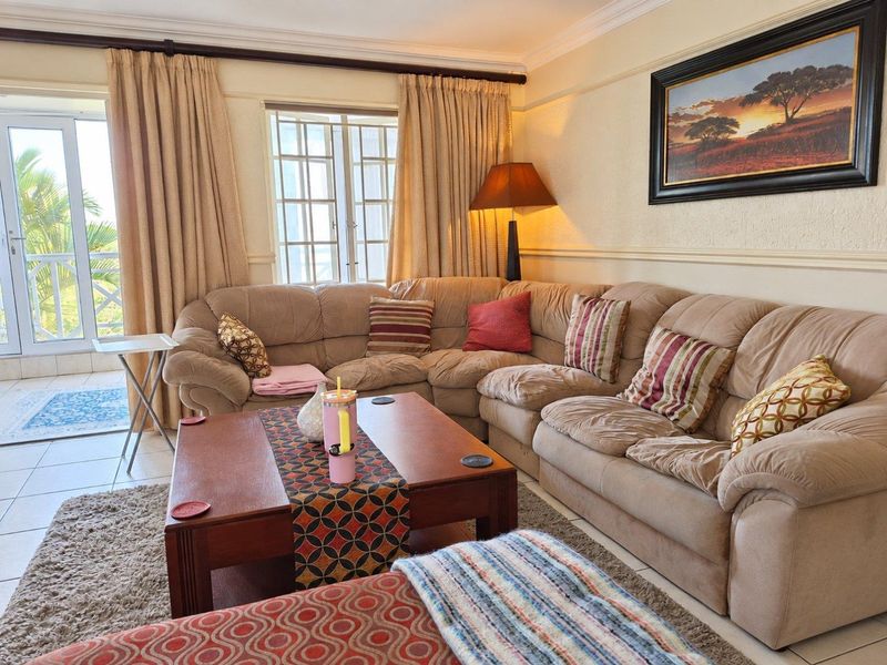 A comfortable living room featuring tiled flooring, cove molding, and direct access to an outdoor balcony through a glass sliding door.