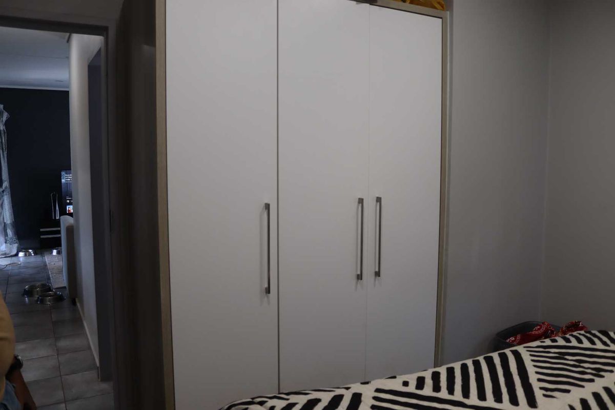 A bedroom featuring a large, modern built-in wardrobe with clean white doors and sleek metal handles.