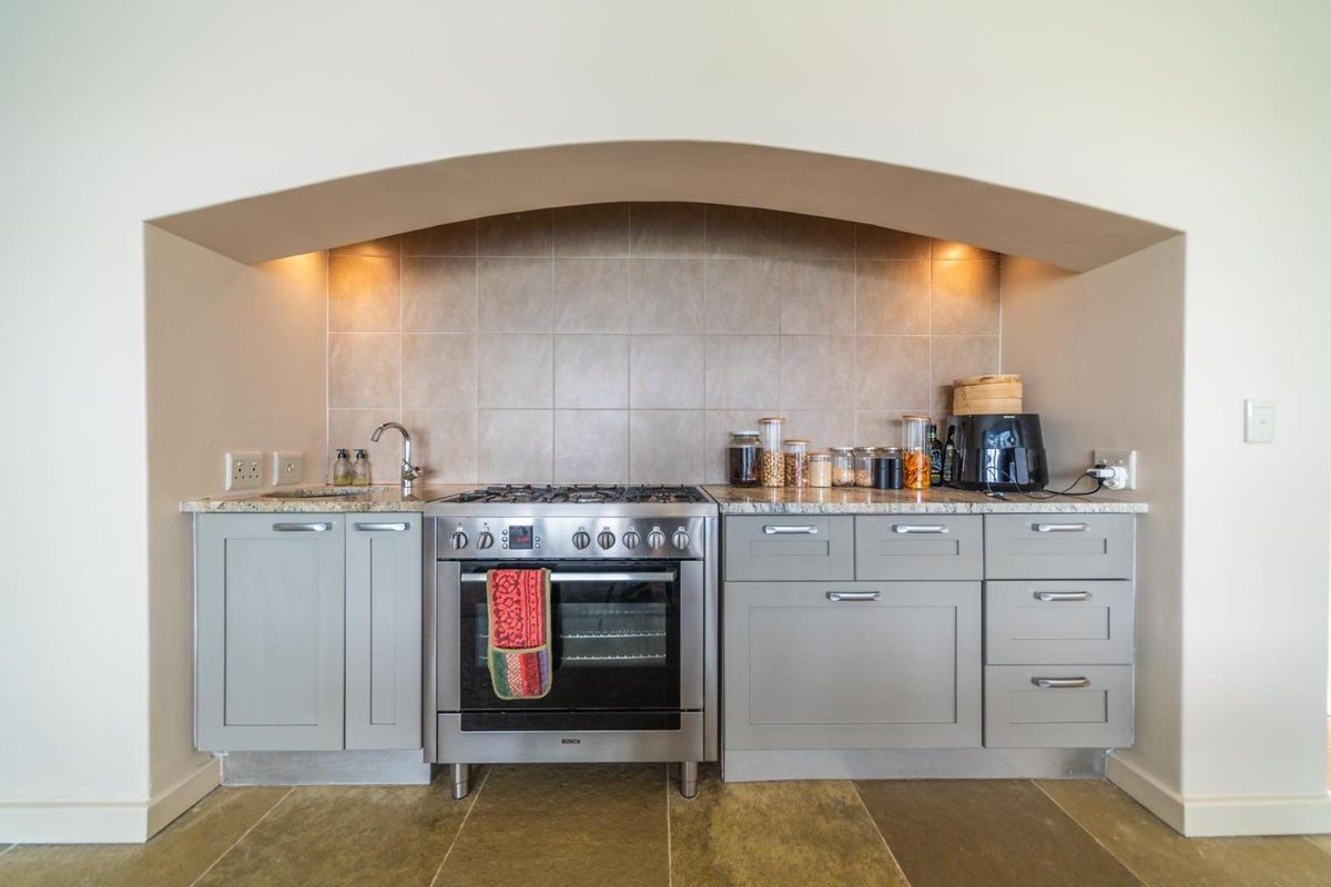 A well-appointed kitchen alcove featuring a stainless steel gas stove, granite countertops, tiled backsplash, and modern grey cabinetry with integrated lighting.