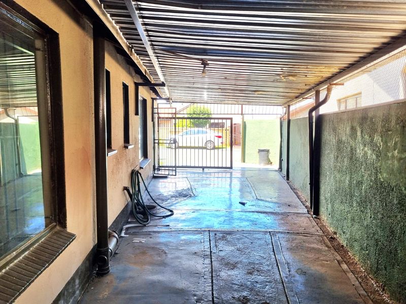 A covered outdoor parking area or carport featuring a corrugated metal roof, concrete flooring, and a secure metal gate entrance.