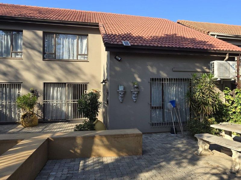 Rear view of the townhouse featuring a paved patio area, security-fitted sliding doors, and a terracotta tiled roof.