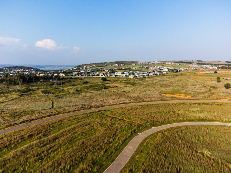 An aerial view of the surrounding landscape and neighborhood, showcasing the local terrain, paved access roads, and nearby residential development.