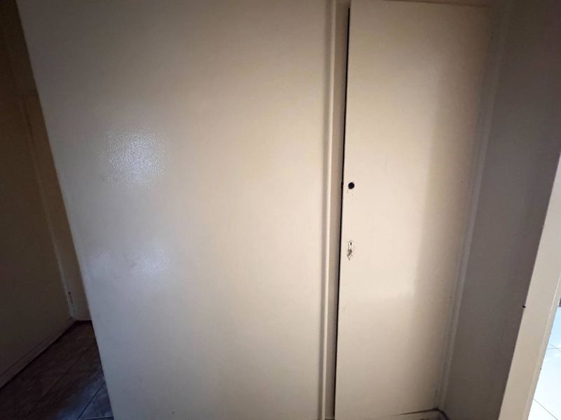 A narrow hallway area featuring a built-in cupboard with a missing handle.