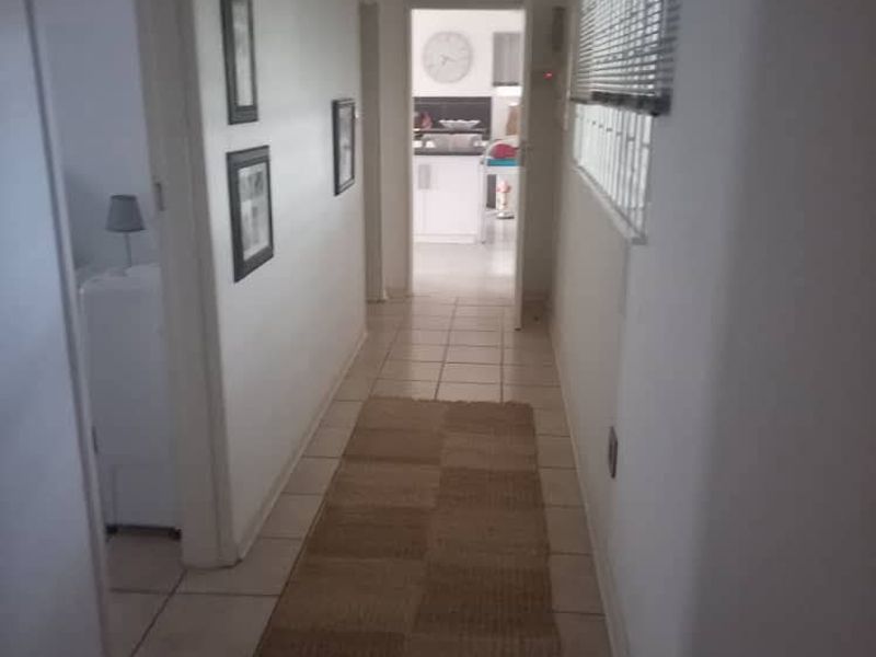 A functional hallway featuring tiled flooring and a window with venetian blinds, providing access to adjacent rooms.