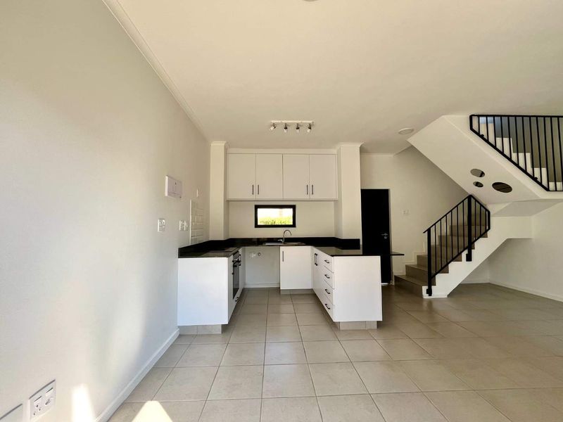 Open-plan kitchen featuring white cabinetry, stone countertops, and integrated appliances, seamlessly flowing into the living area with a staircase leading to the upper level.