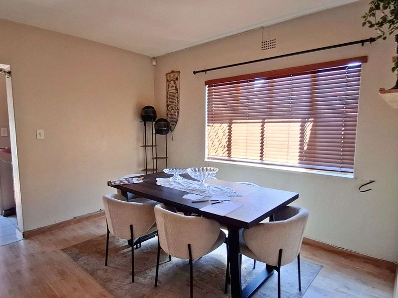 A dining room featuring laminate flooring and venetian blinds, with access to an outdoor area. The space requires minor maintenance to skirting and electrical finishes.