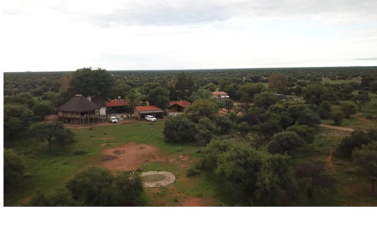 Aerial view of a farm property featuring multiple structures, a thatched-roof main dwelling, and a small water feature set within a vast landscape.