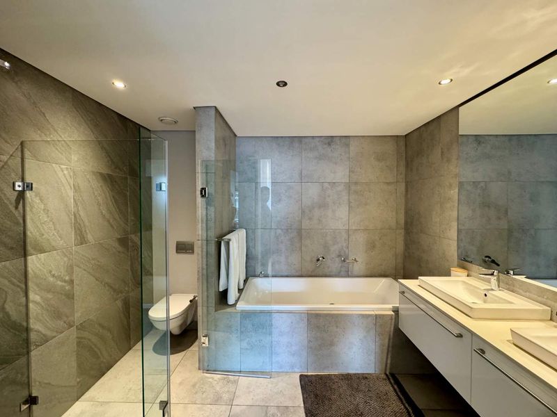 Modern bathroom featuring a glass-enclosed shower, built-in bathtub, wall-mounted toilet, and a sleek double vanity with large mirror and contemporary tile finishes.