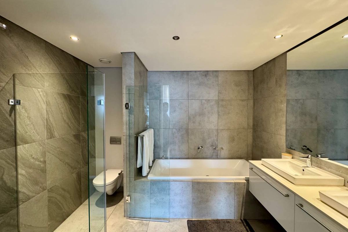 Modern bathroom featuring a glass-enclosed shower, built-in bathtub, wall-mounted toilet, and a sleek double vanity with large mirror and contemporary tile finishes.