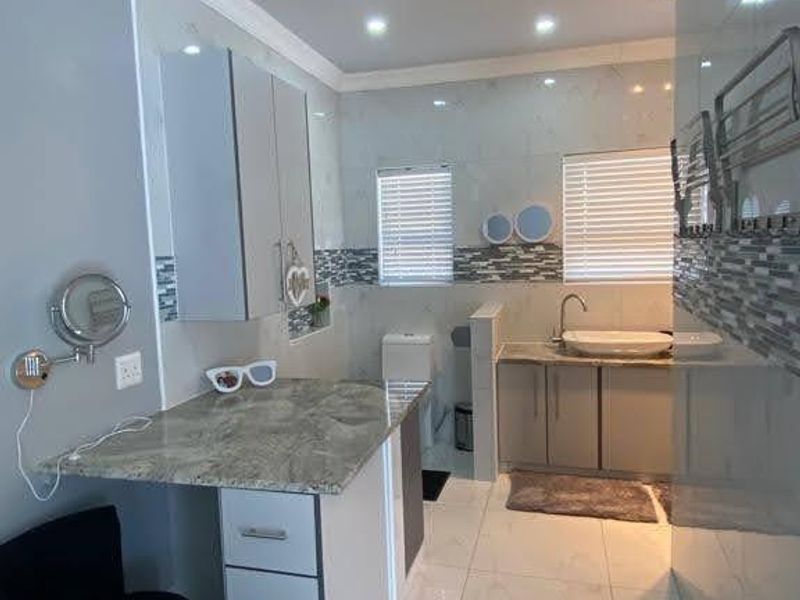 A modern, well-lit bathroom featuring tiled walls and floors, a stone-topped vanity with integrated sink, and a private toilet area.