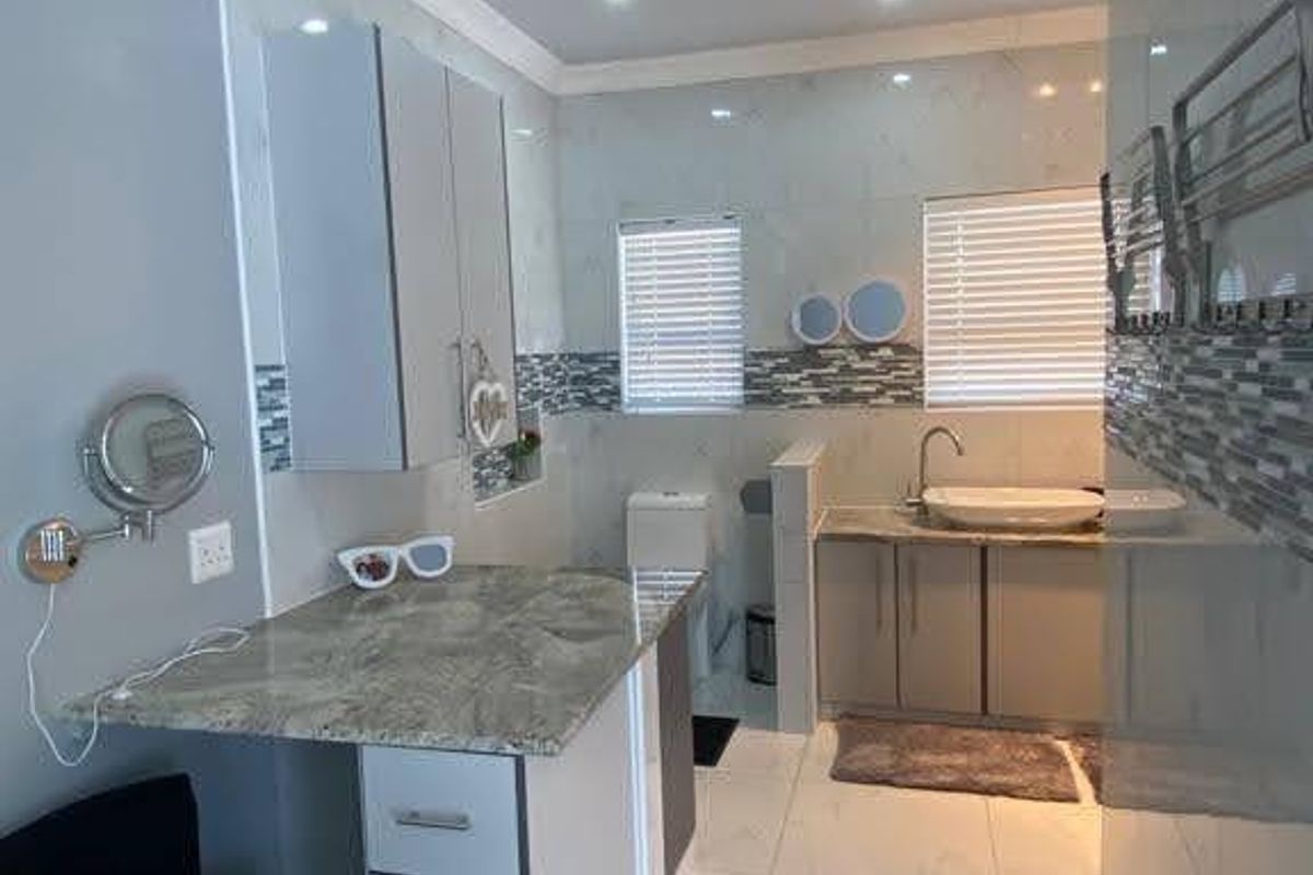 A modern, well-lit bathroom featuring tiled walls and floors, a stone-topped vanity with integrated sink, and a private toilet area.