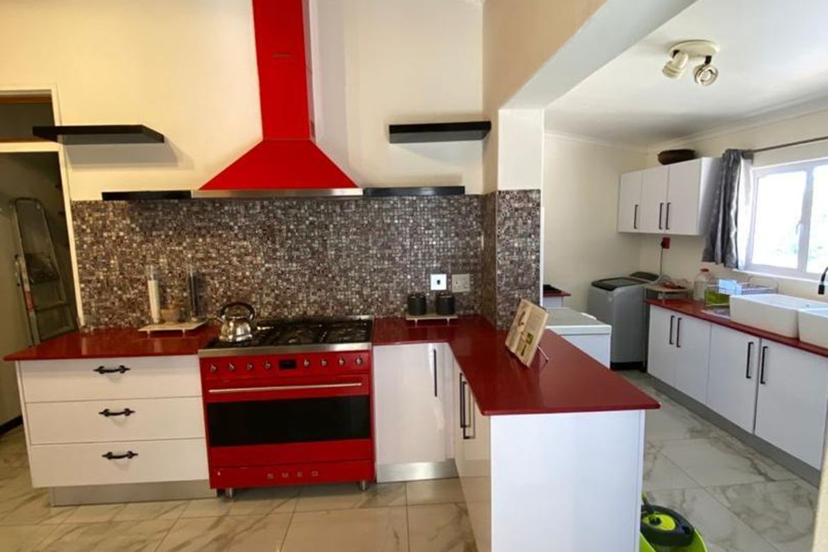 Modern kitchen featuring a striking red Smeg range cooker, matching extractor, mosaic backsplash, and marble-look tiled flooring under a vaulted timber ceiling.