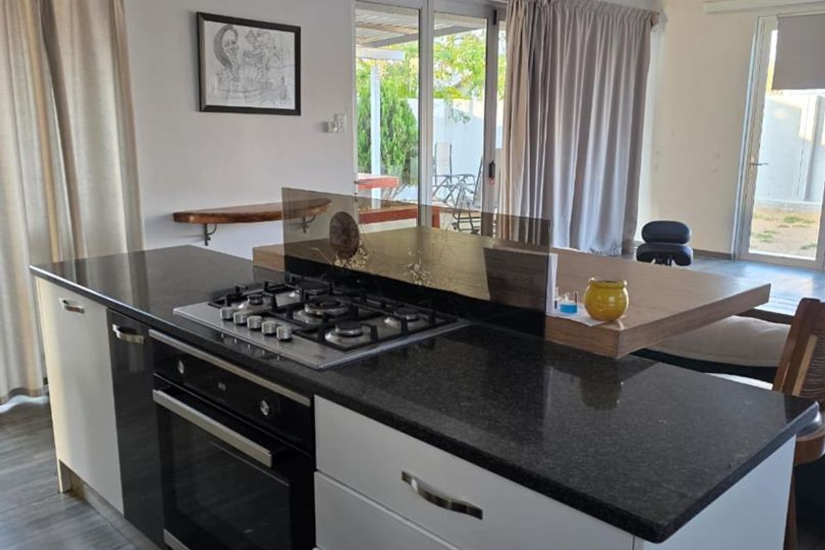 Modern kitchen island featuring a gas hob, built-in oven, granite countertops, and an integrated timber breakfast bar, opening onto an outdoor patio area.