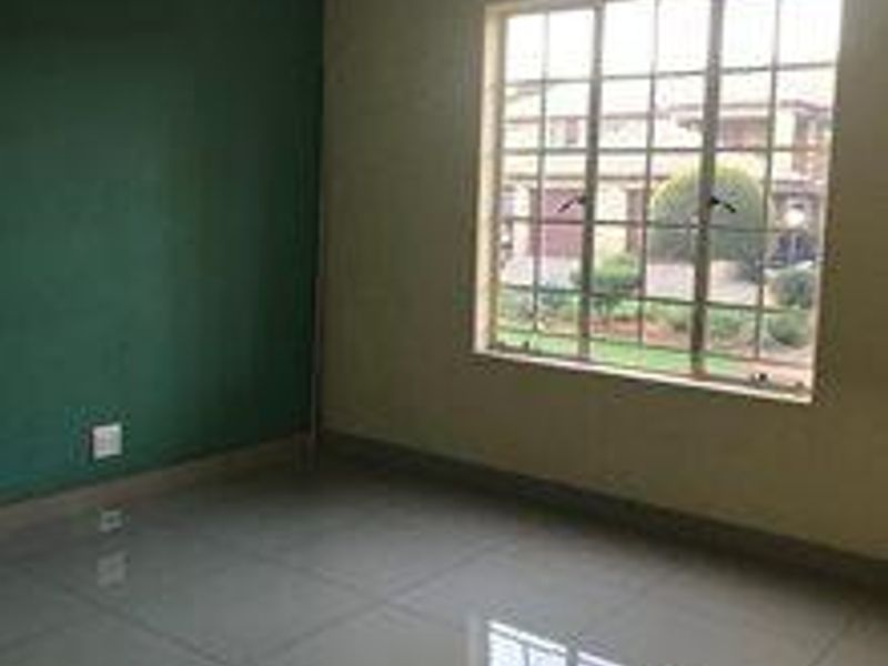 An empty bedroom featuring large tiled flooring, a grid-pattern window, and a green accent wall, offering a blank canvas for personalization.