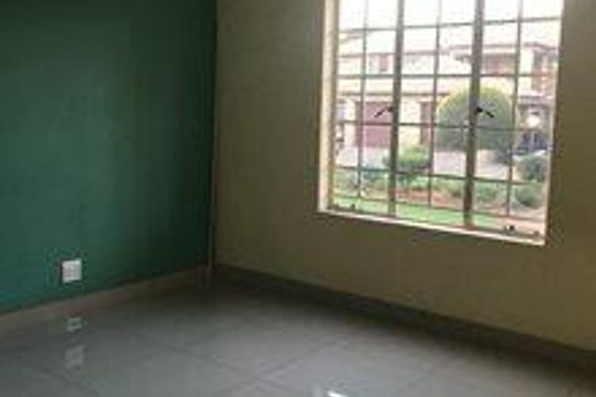 An empty bedroom featuring large tiled flooring, a grid-pattern window, and a green accent wall, offering a blank canvas for personalization.