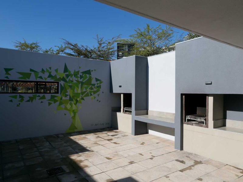 A spacious outdoor patio area featuring a built-in braai, concrete bench seating, and tiled flooring, perfect for outdoor entertaining.