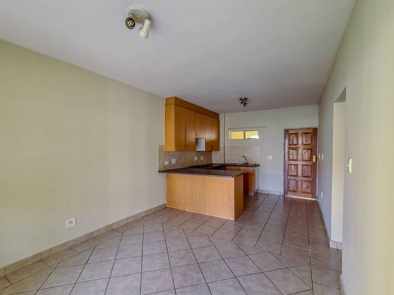 An open-plan kitchen and living area featuring tiled flooring, built-in wooden cabinetry, and a solid wood entrance door.