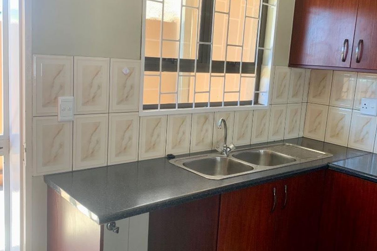 A functional kitchen area featuring dark wood-finish cabinetry, a double-basin stainless steel sink, and a tiled backsplash with a security-barred window.