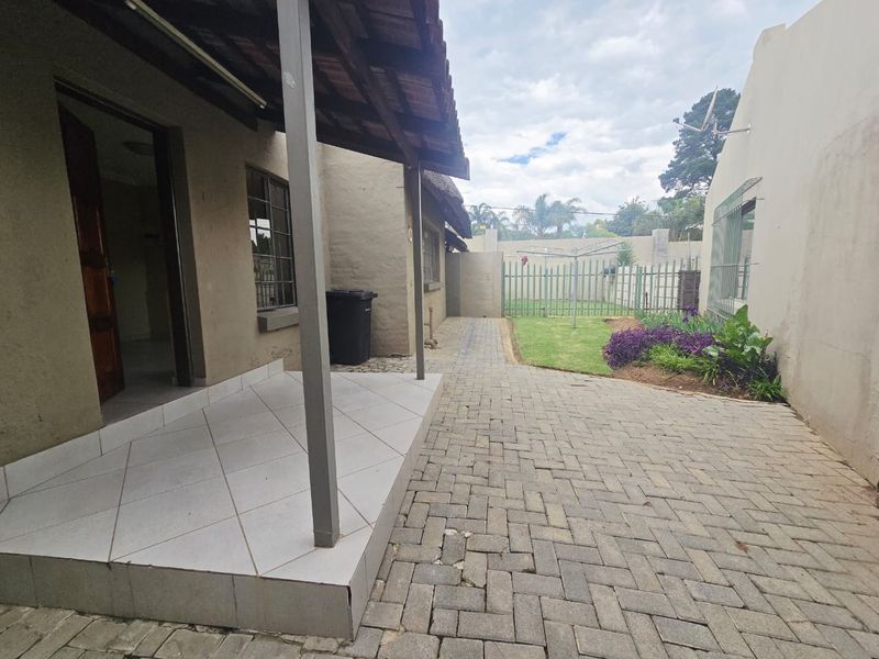 Rear exterior view of the cottage featuring a tiled patio, paved courtyard area, and a small garden with security fencing.