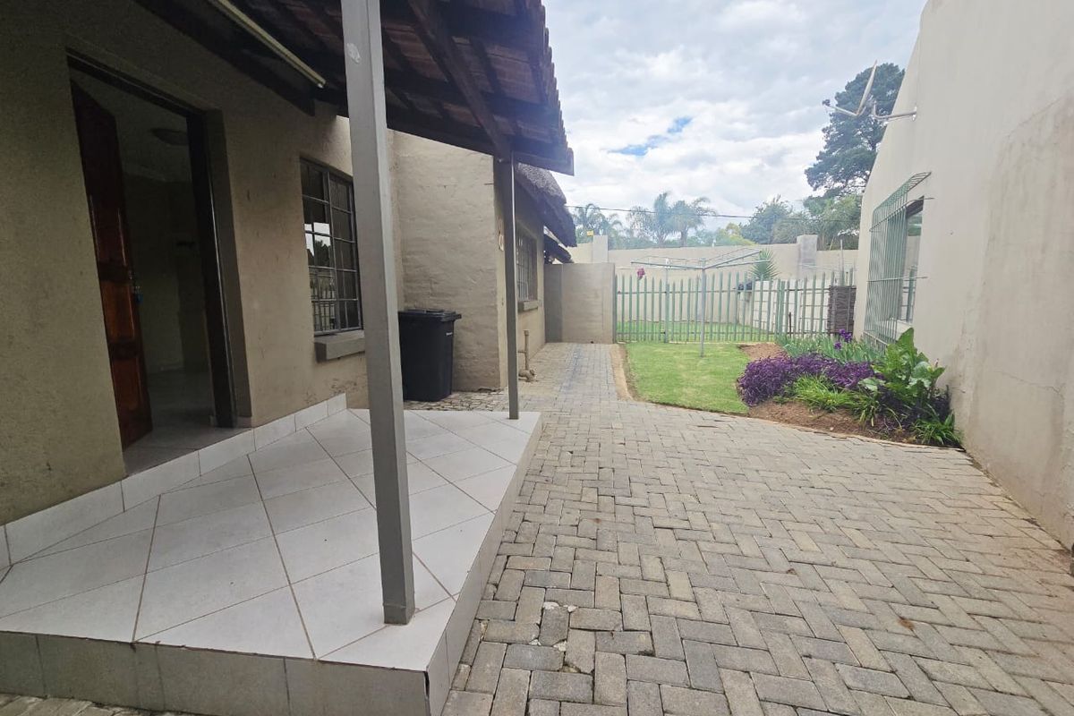 Rear exterior view of the cottage featuring a tiled patio, paved courtyard area, and a small garden with security fencing.