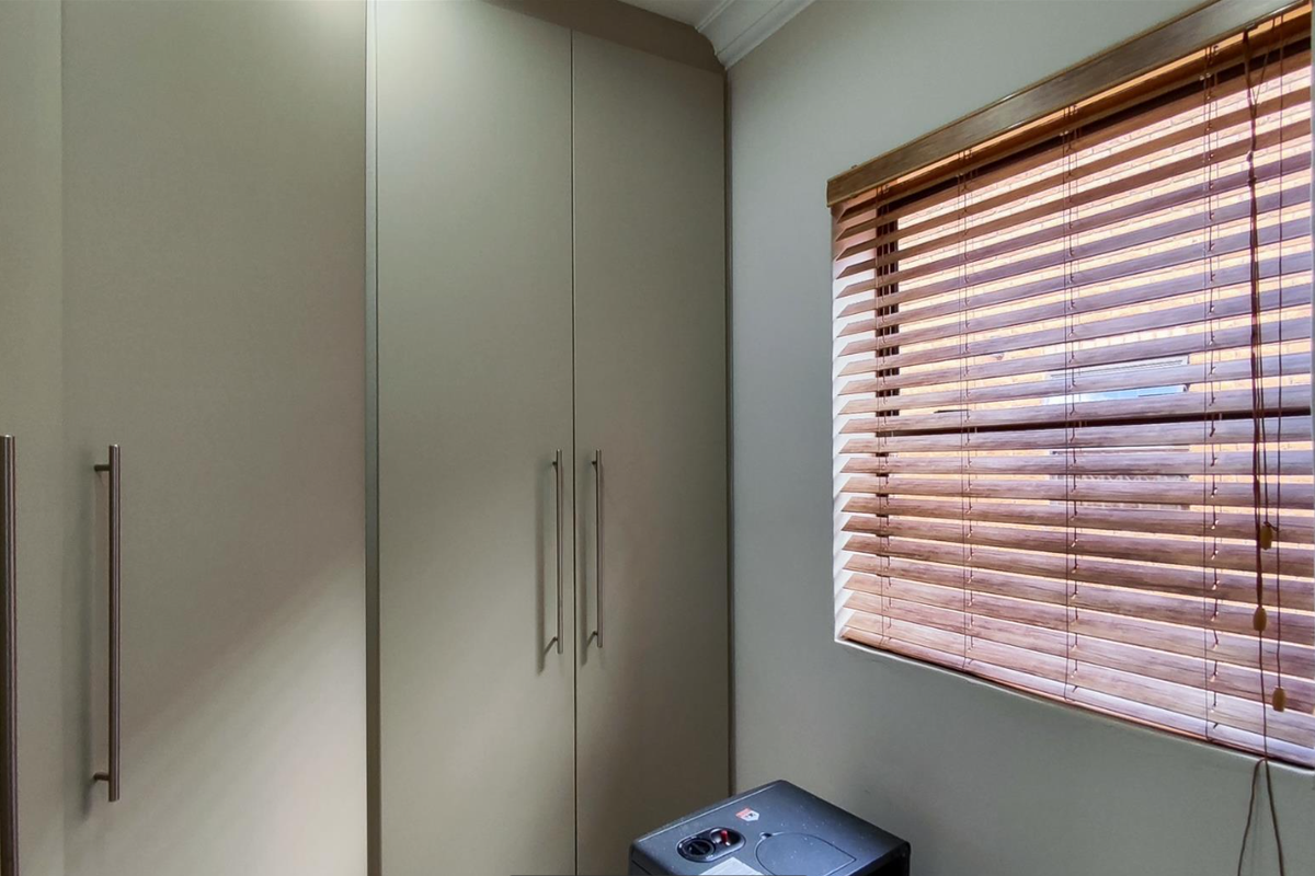 A well-maintained bedroom featuring built-in floor-to-ceiling cabinetry and a window fitted with wooden venetian blinds.