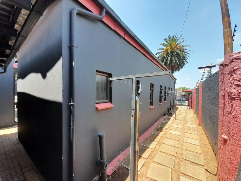 A side exterior view of the property featuring a paved walkway, boundary wall, and external drainage infrastructure.
