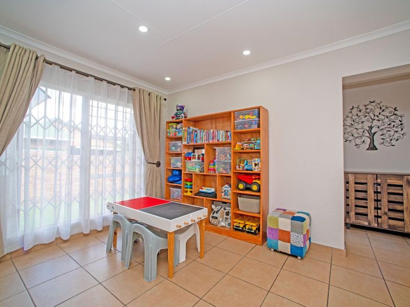 A bright living area featuring neutral tiled flooring, recessed downlighting, and a sliding glass door with security gate leading to the exterior.