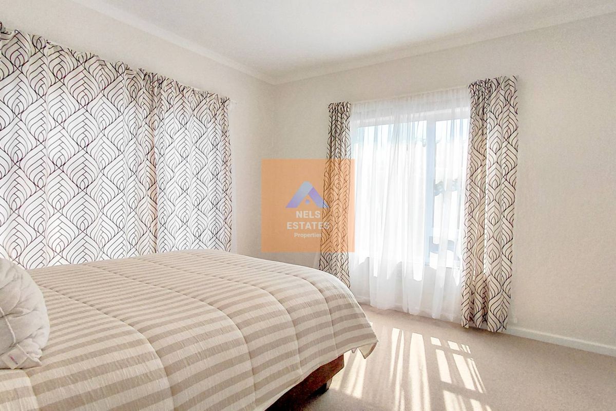 A bright and neutral bedroom featuring carpeted flooring and large windows with installed curtain rails.