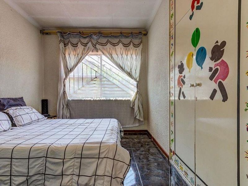 A bedroom featuring tiled flooring, a built-in wardrobe, and security bars on the window.
