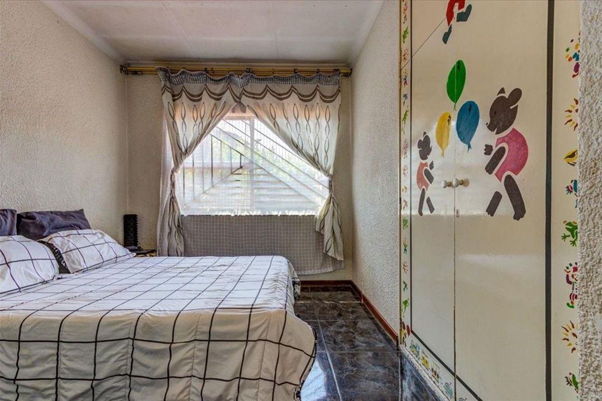 A bedroom featuring tiled flooring, a built-in wardrobe, and security bars on the window.