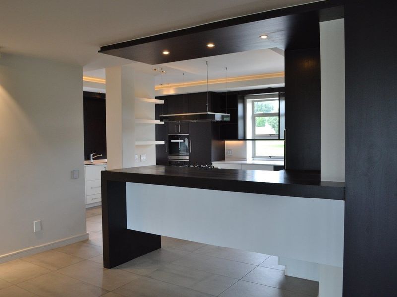 Modern open-plan kitchen featuring a sleek breakfast bar, built-in appliances, recessed lighting, and high-quality tiled flooring in a contemporary apartment setting.