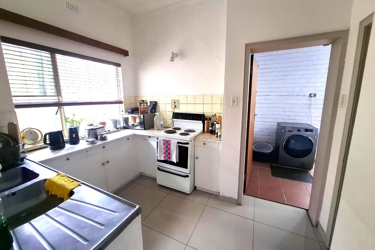 Functional kitchen featuring white cabinetry, tiled backsplash, and a freestanding stove, with an adjacent laundry area visible through the doorway.