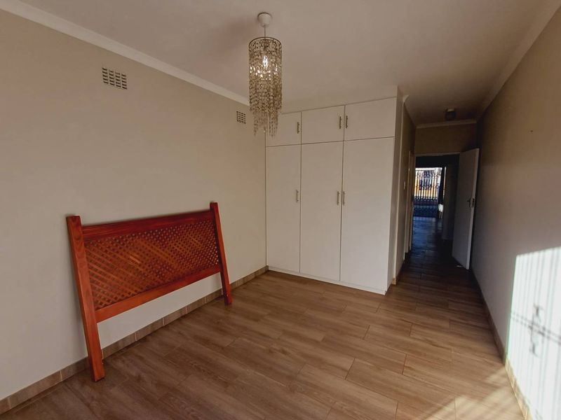 A bright, empty bedroom featuring modern laminate flooring, neutral walls, and ample built-in cupboard storage space.