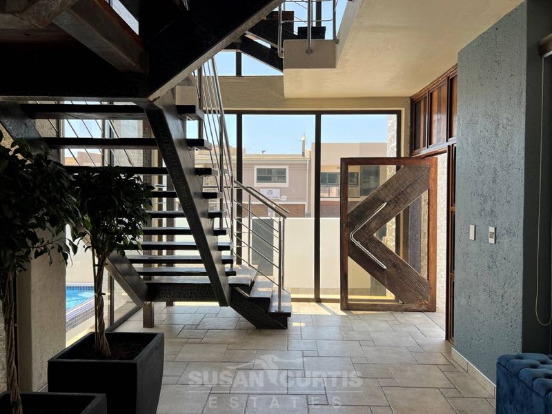 Modern entrance hall featuring a striking steel staircase, large format floor tiles, and a statement pivot door with expansive glass panels.
