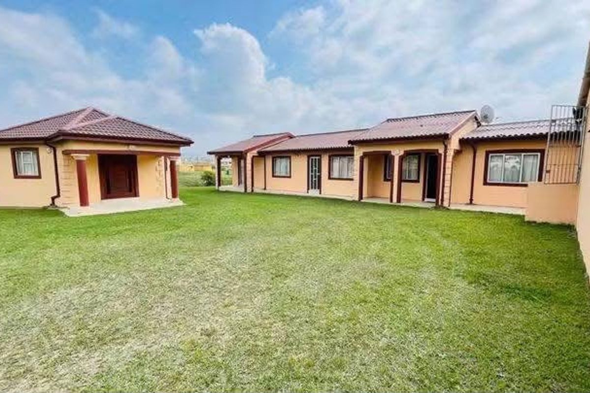 A spacious rear garden area featuring multiple detached building structures with tiled roofs and covered patio sections.