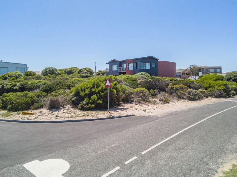 A street-level view of the residential vacant land, featuring paved road access, kerbing, and surrounding coastal vegetation in a quiet neighborhood setting.