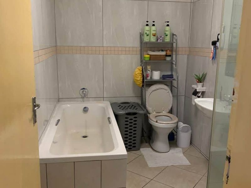 A functional bathroom featuring a bathtub, toilet, and wall-mounted basin with neutral tiled finishes throughout.