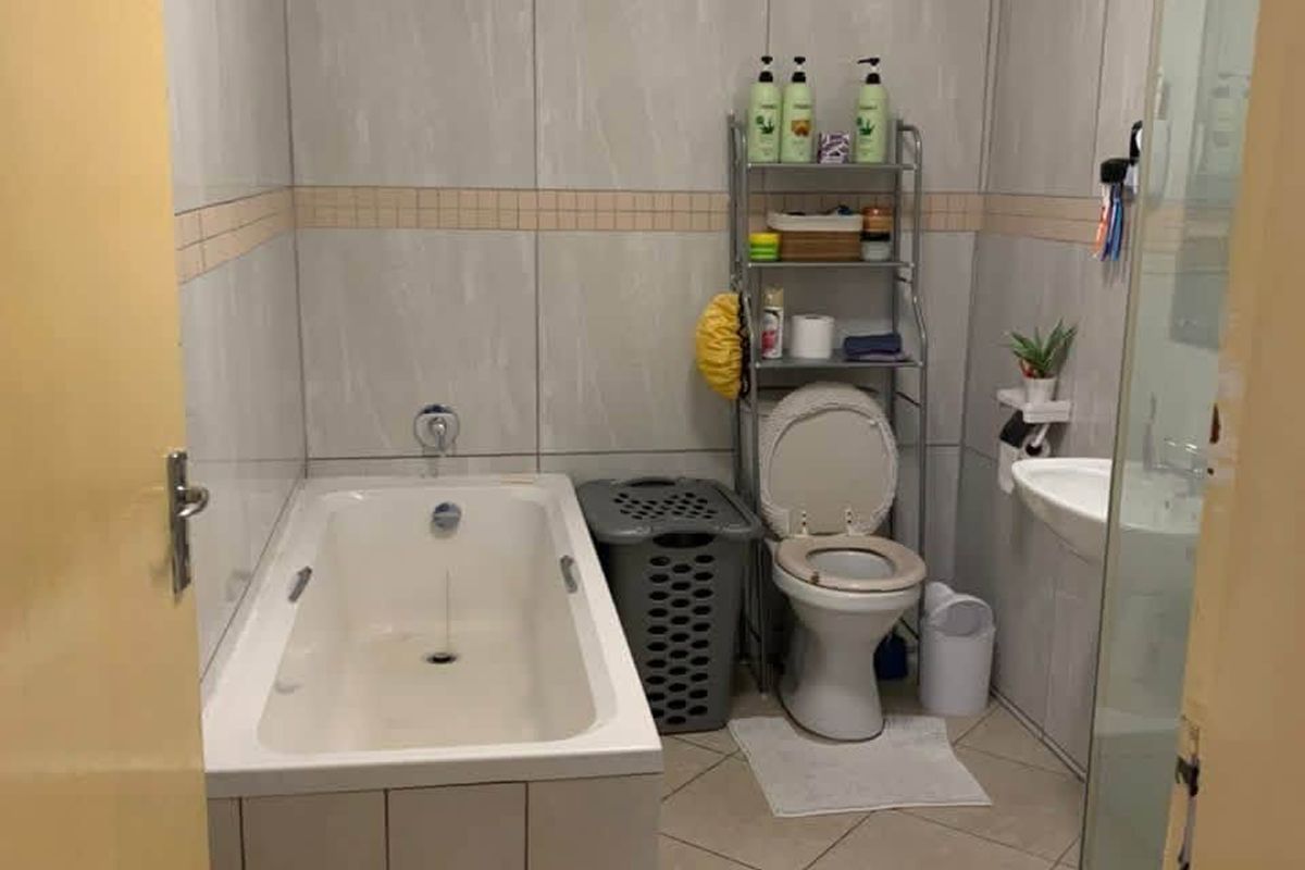 A functional bathroom featuring a bathtub, toilet, and wall-mounted basin with neutral tiled finishes throughout.