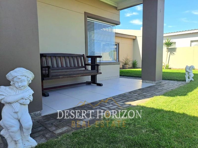 A well-maintained covered patio area featuring tiled flooring, overlooking a neat garden with paved pathways.