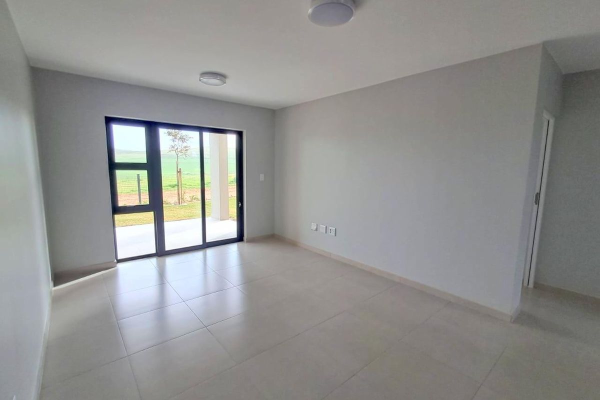 A bright, empty living area featuring neutral tiled flooring, modern flush-mount ceiling lights, and large sliding glass doors leading to an outdoor space.