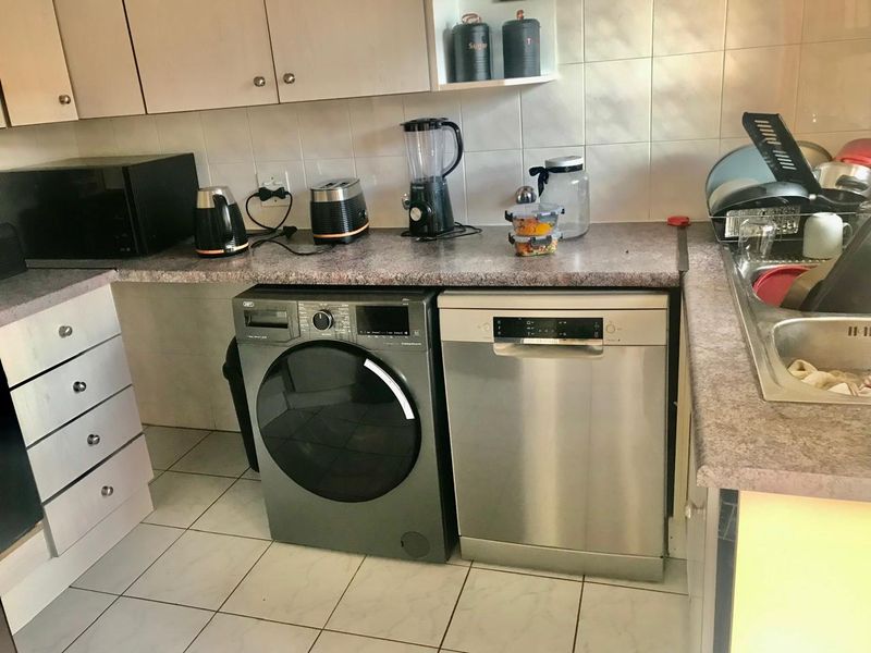A functional kitchen area featuring laminate countertops, tiled backsplash, built-in cabinetry, and tiled flooring with space for under-counter appliances.