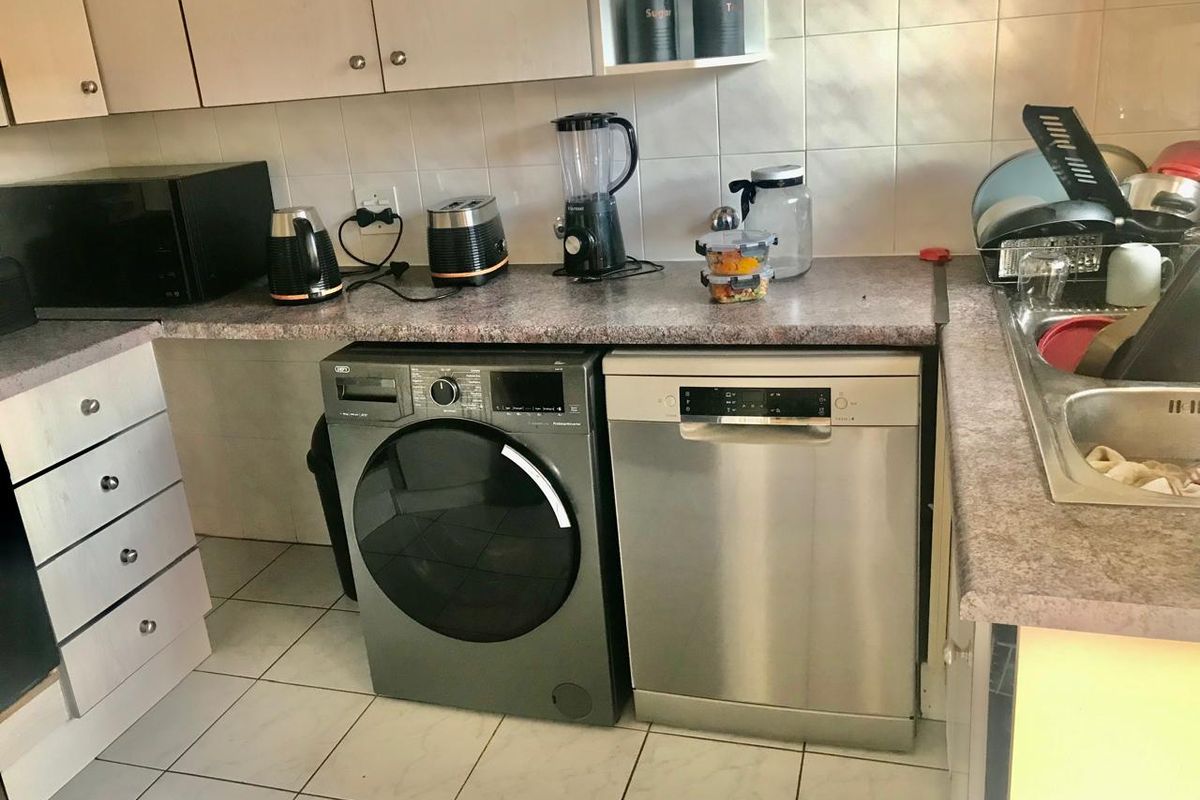 A functional kitchen area featuring laminate countertops, tiled backsplash, built-in cabinetry, and tiled flooring with space for under-counter appliances.