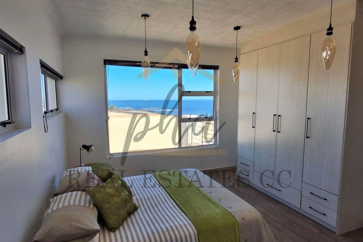 A bright bedroom featuring built-in floor-to-ceiling wardrobes, modern pendant lighting, and a large window offering expansive ocean views.