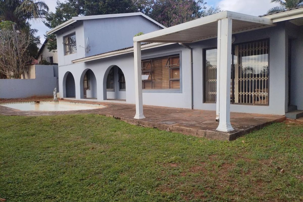 Rear exterior view featuring a swimming pool, a covered patio area with arched architectural details, and a paved terrace overlooking the garden.