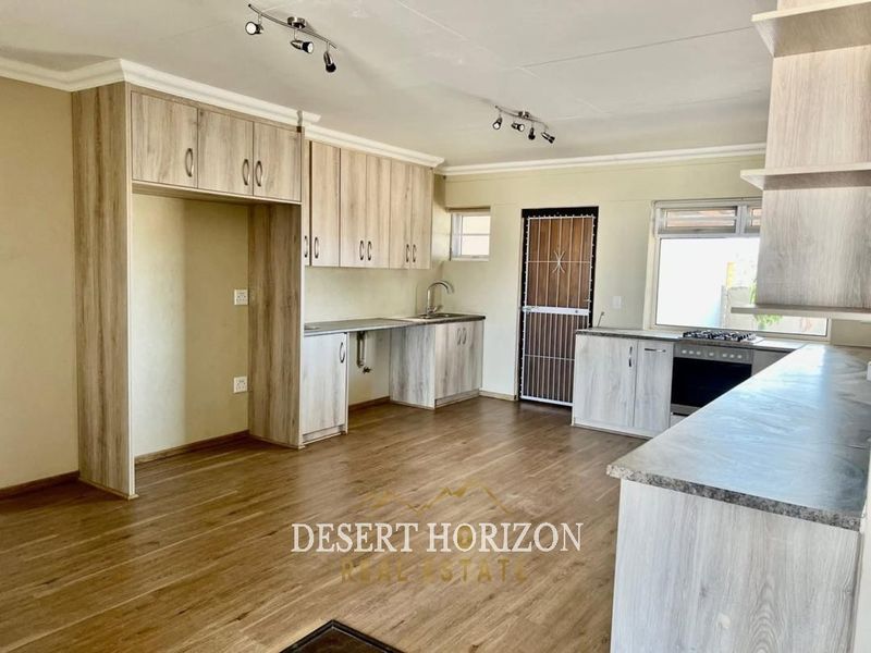 A clean, empty kitchen featuring light wood-look cabinetry, laminate countertops, built-in oven and hob, and durable laminate flooring.